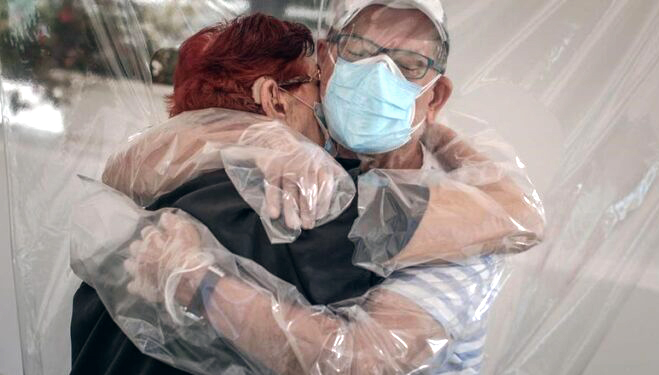 Fotografía. Un matrimonio abrazándose con una cortina de plástico, parte del protocolo anti COVID, separando sus cuerpos.