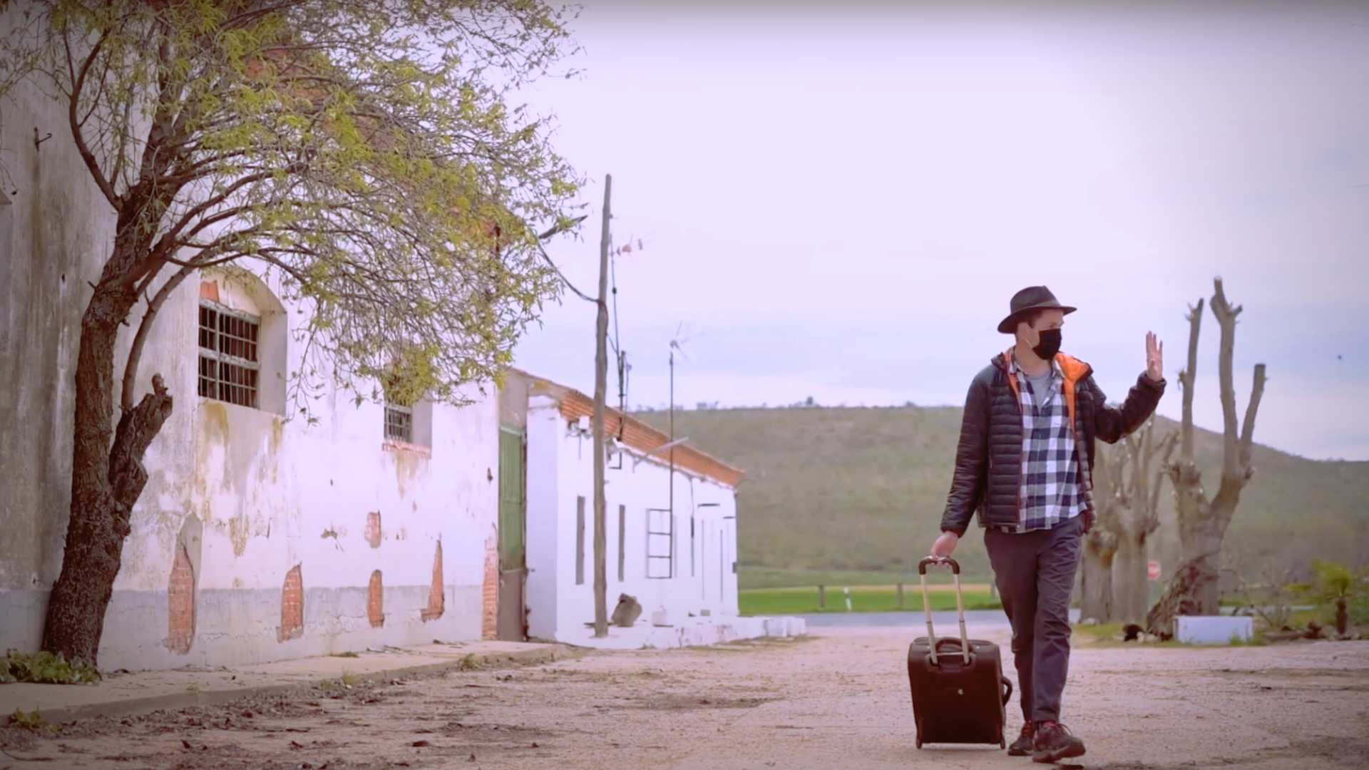 Película. Vista frontal de Raúl Aguirre con una maleta de ruedas, despidiéndose de su pueblo natal.