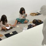 Detalle de la escultura 'Xurxo'. En la misma sala, frente a ella, el grupo infantil realiza collages sobre cartulinas en el suelo.
