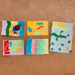 Vista superior de cinco manualidades realizadas en cartulinas de diferentes colores. Sobre éstas, collages de figuras abstractas, inspirados en las obras de Gillian Ayres.