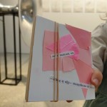 Vista detalle de una mano mostrando un cuaderno pequeño de arte creado a mano con papel celofán rosa, lentejuelas, recortes de papel con formas geométricas y palabras superpuestas.