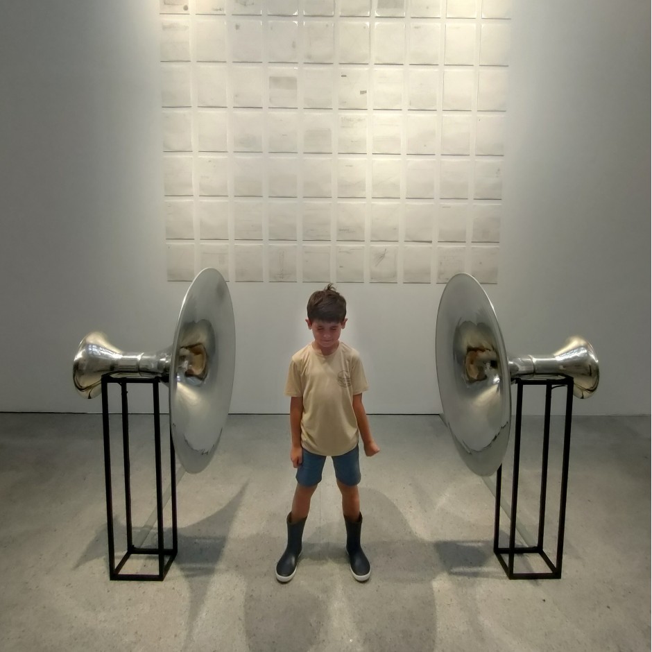Vista frontal de un menor en el centro de dos esculturas en forma de megáfonos. Las esculturas pertenecen a la obra «Hablar y responder. Tres improvisaciones para Rayuela», de Tania Candiani.