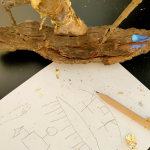 Sobre una mesa, detalle de la recreación en madera de la obra ‘Barca con cofre’  junto a un dibujo a lápiz.