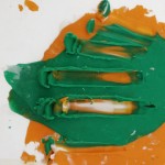 Detalle. Sobre un fondo claro, una mancha de pintura verde sobre una mancha de pintura naranja.