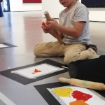 Detalle del grupo infantil creando en el suelo una obra con cartulinas, pintura y rodillos de cocina.