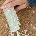 Detalle de una mano infantil tallando material moldeable transparente similar a la cera. 