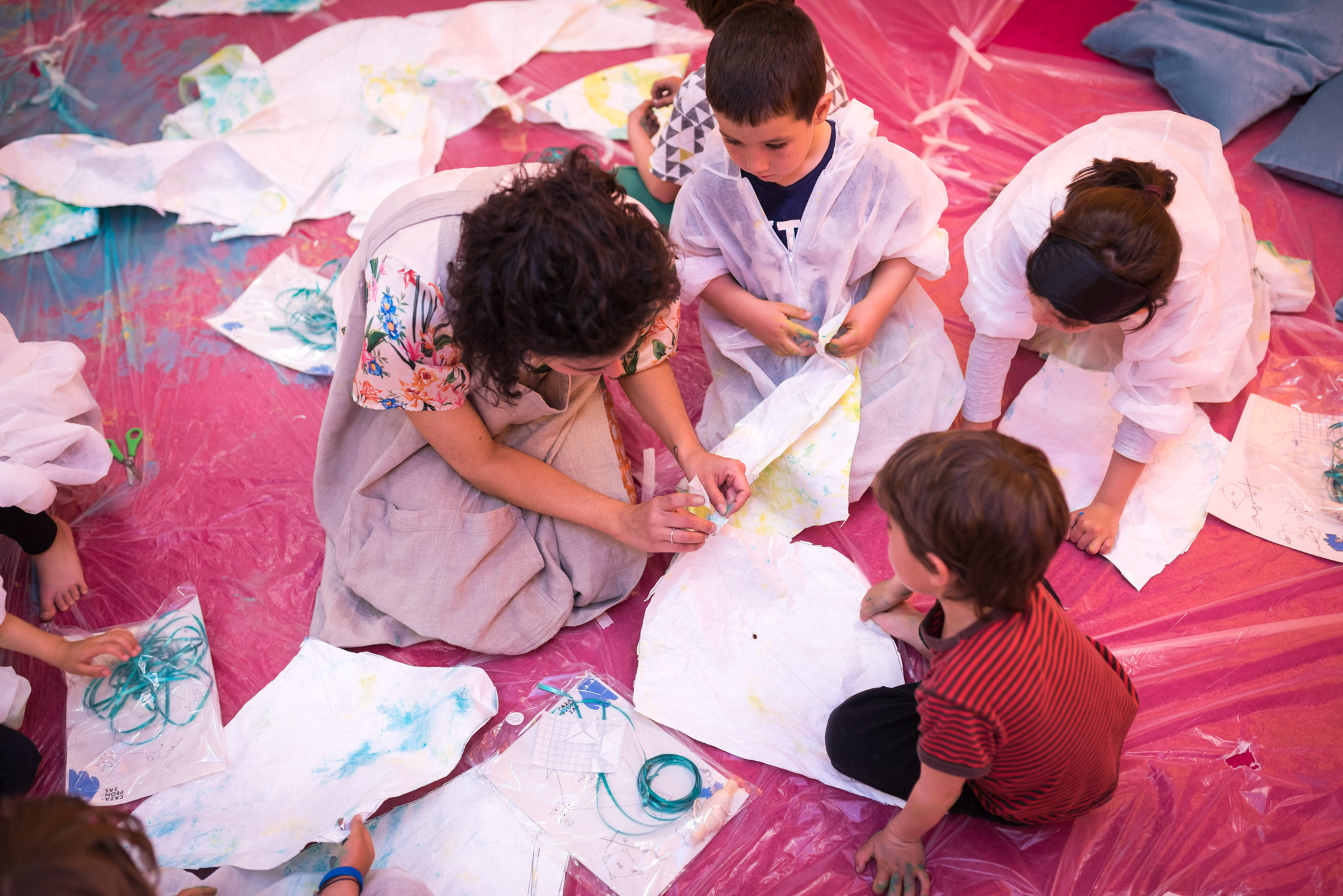 Vista superior de un grupo de niñas y ninos que, junto a María, realizan manualidades con tela y pintura.