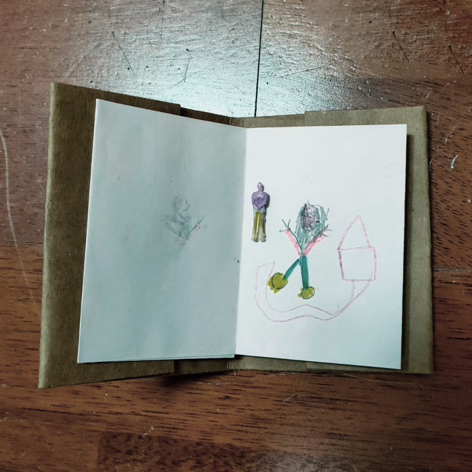 Plano detalle de una carpeta pequeña de cartón abierta con una hoja en la que hay dibujada una persona que parece abandonar su hogar. Sobre el dibujo, una pequeña figurita en forma de persona.
