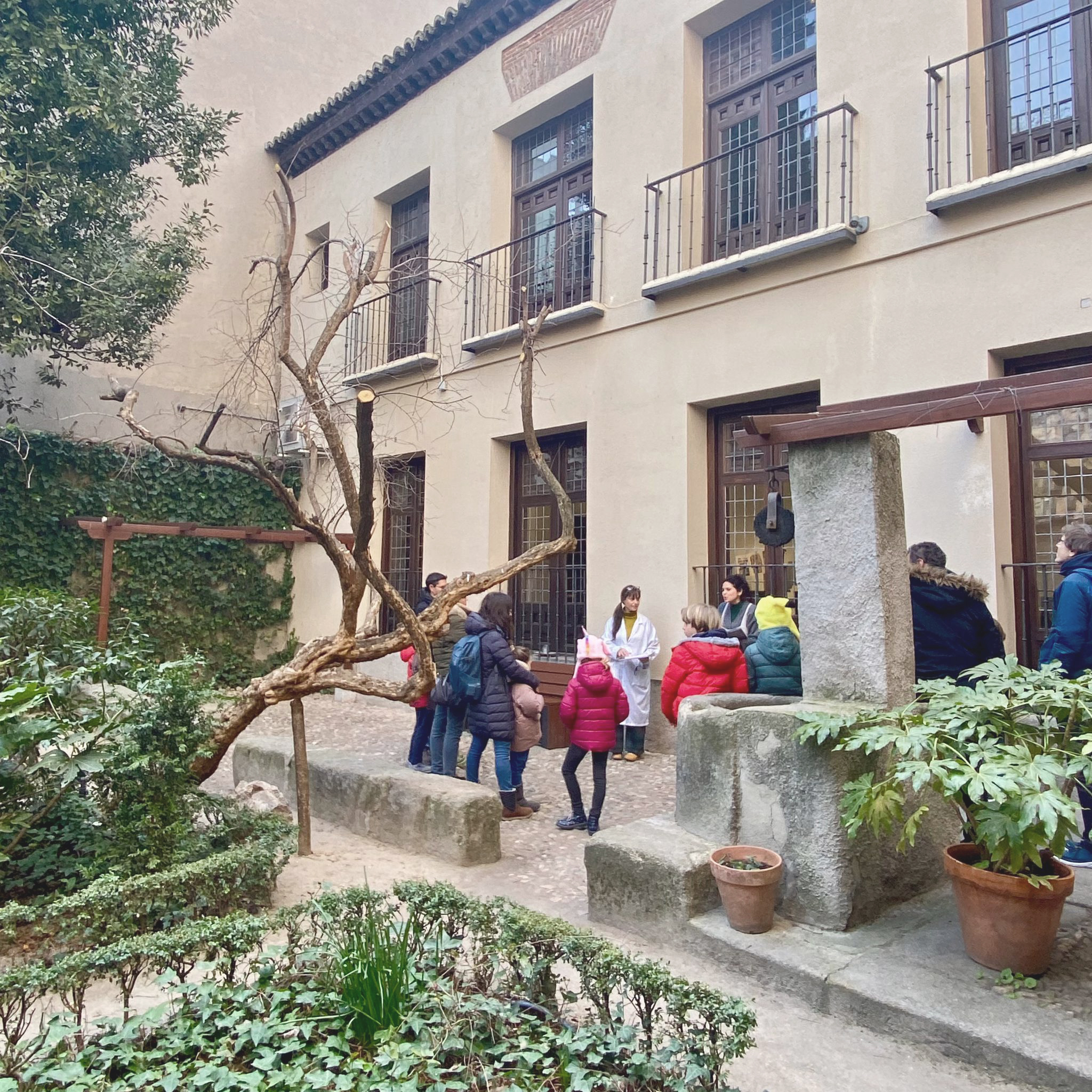 Vista general. Un grupo de 12 personas hablando en los jardines de Casa Museo Lope de Vega.