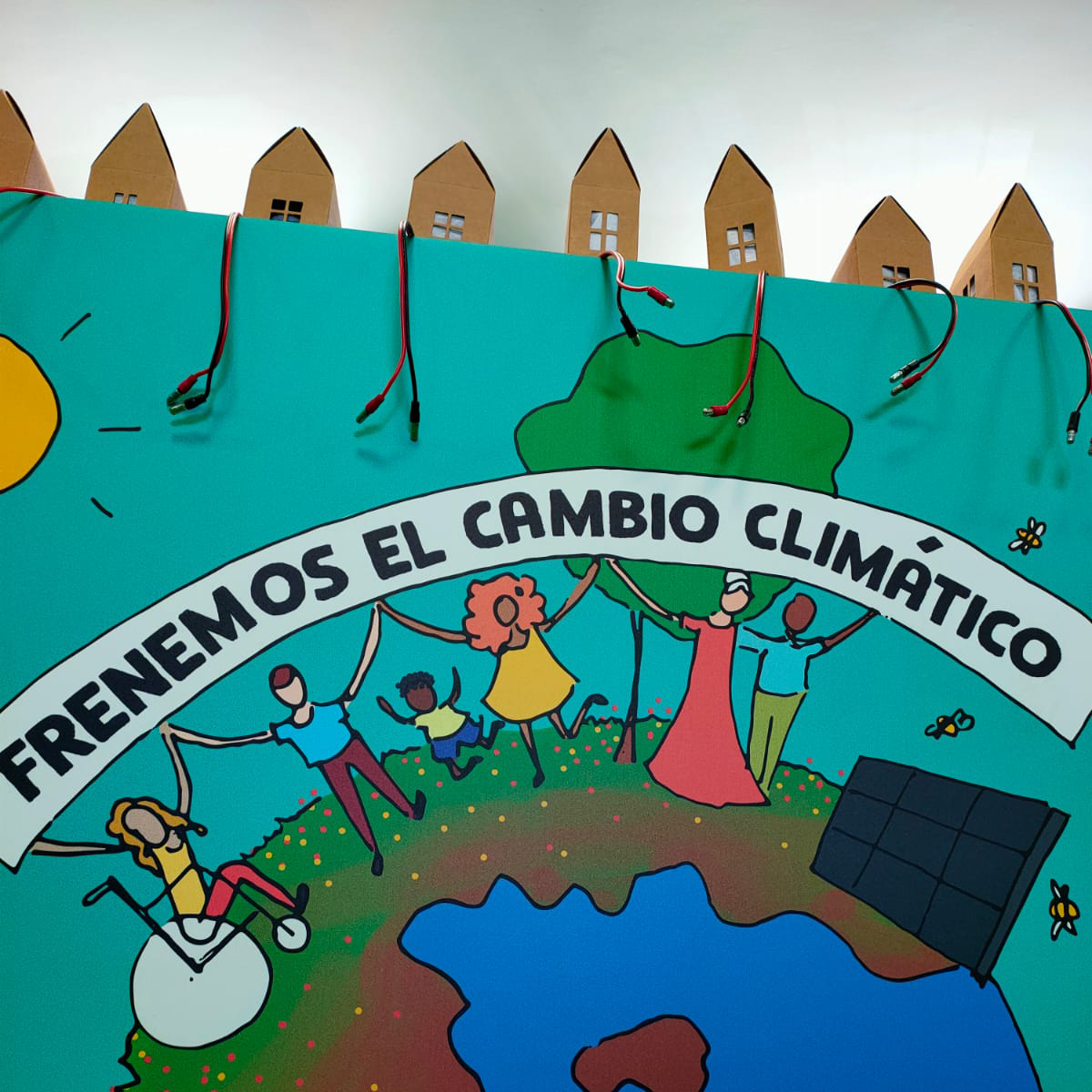 Plano detalle de un cartel con dibujos coloridos del planeta tierra. Sobre la Tierra, una placa solar, personas con las manos unidas y la frase: «Frenemos el cambio climático».