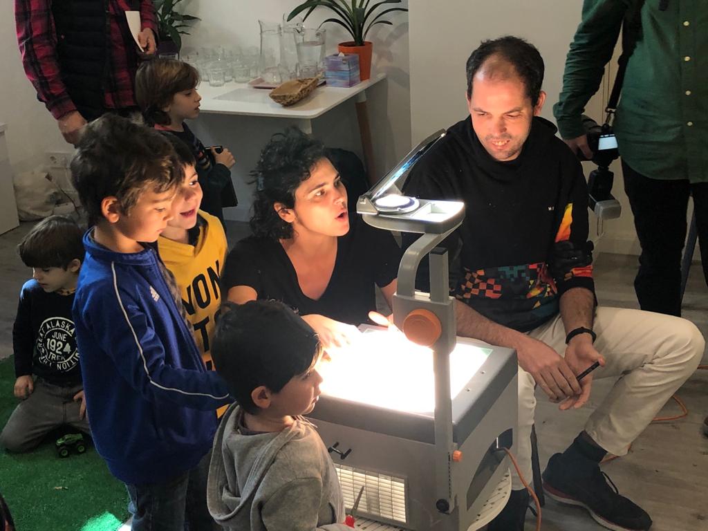Vista lateral de Raúl firmando un libros sobre una mesa con rotuladores y papeles.
