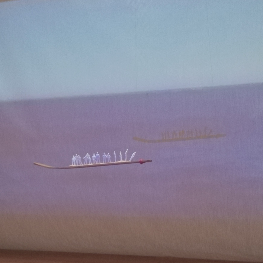 Vista lateral de Raúl firmando un libros sobre una mesa con rotuladores y papeles.