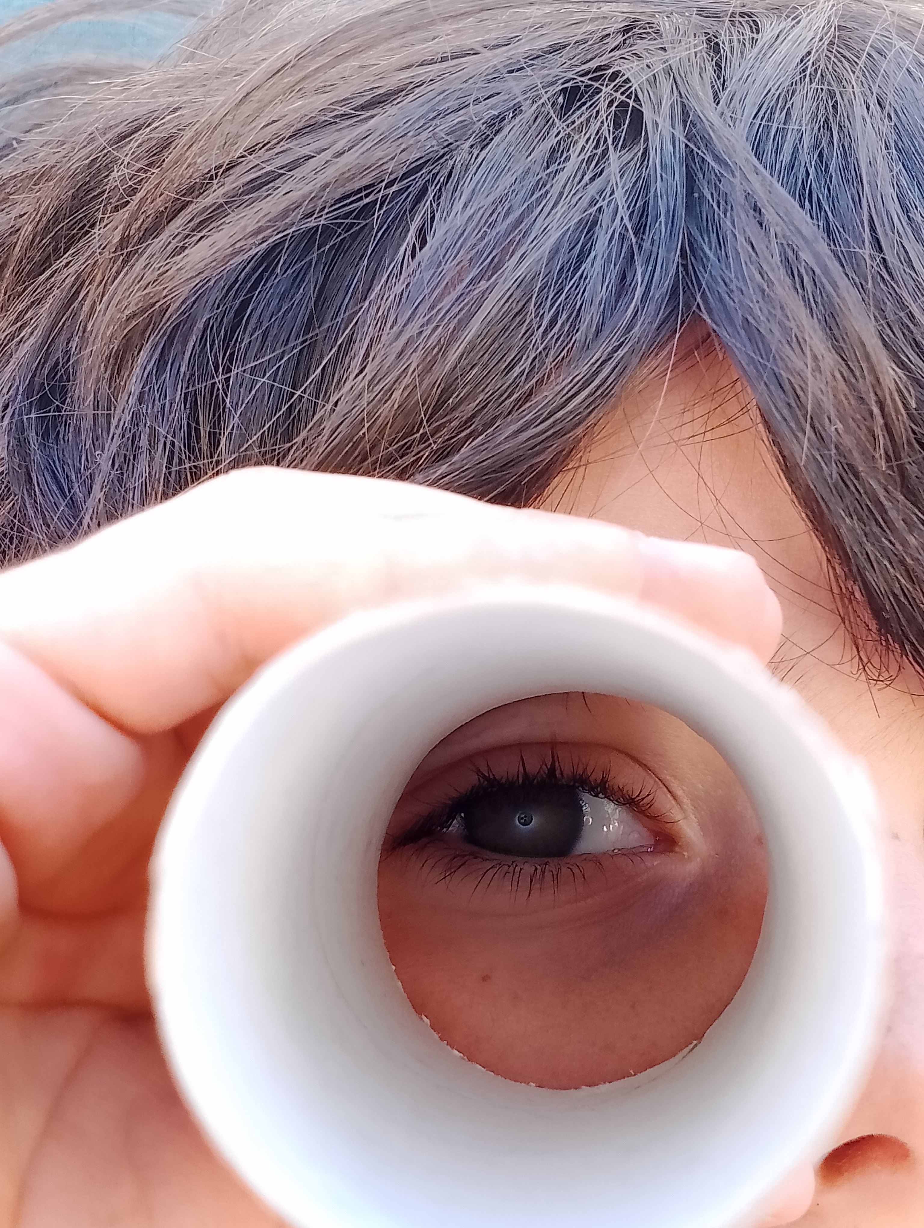 Un niño mirando a través de un rollo de papel. En la foto se ve su ojo a través del rollo