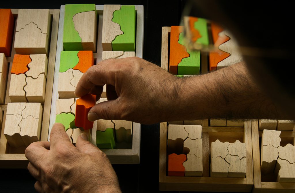 Vista superior de unas manos encajando en la base de un puzle varias piezas de diferente forma y color.